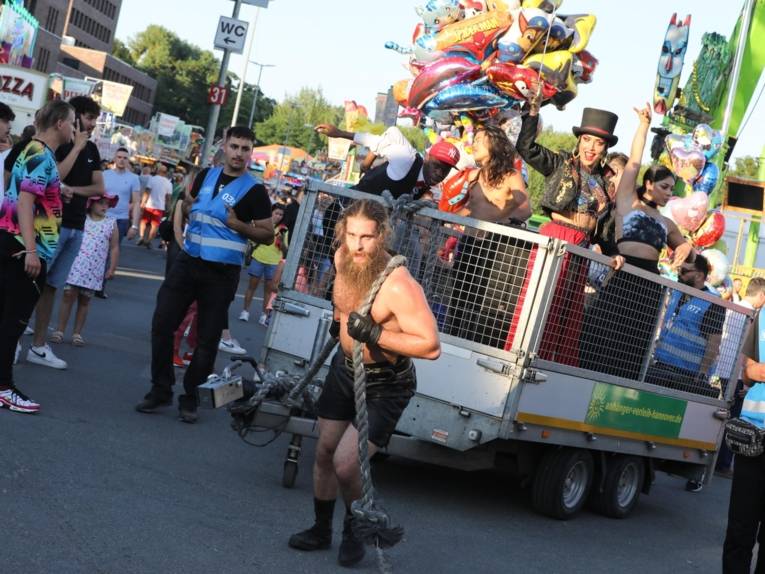 Ein Mann, der einen Wagen mit Artist*innen zieht.